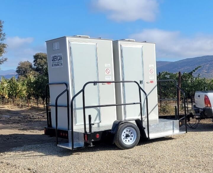 Portable restroom trailer parked on gravel by vineyard rows and hills near Napa, CA